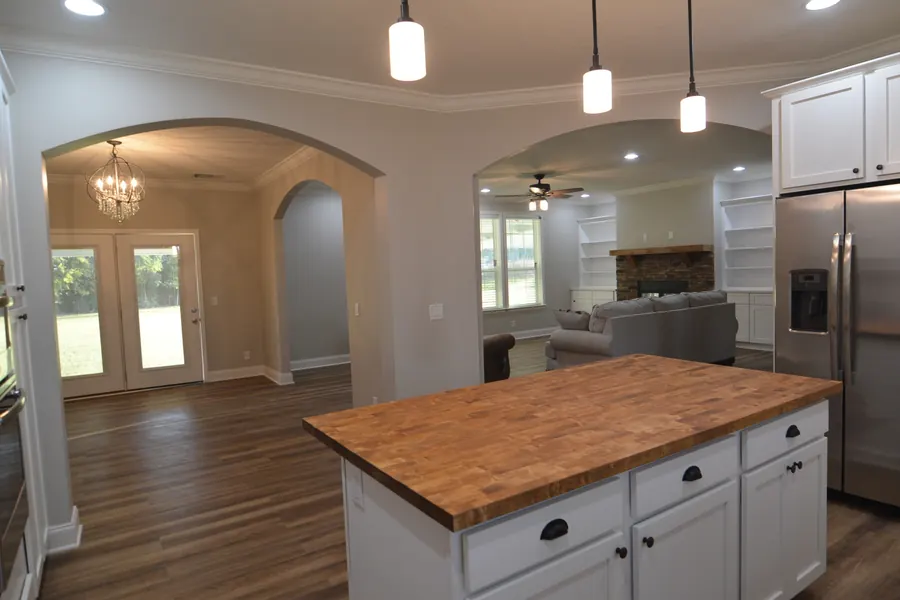 White kitchen with a butcher-block island, pendant lights and arched openings to the living room