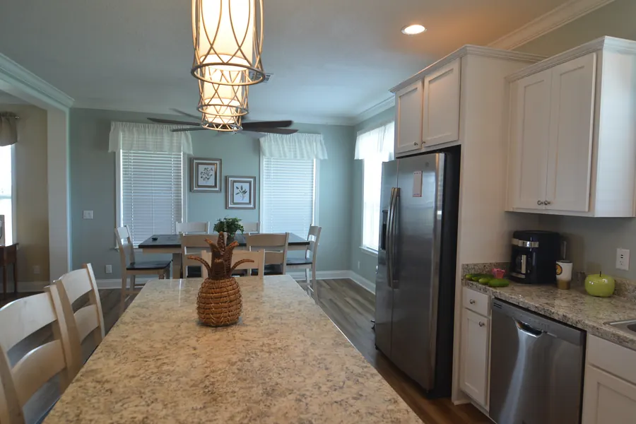 Kitchen with white cabinets, a granite island, stainless appliances and a dining table under a lantern light