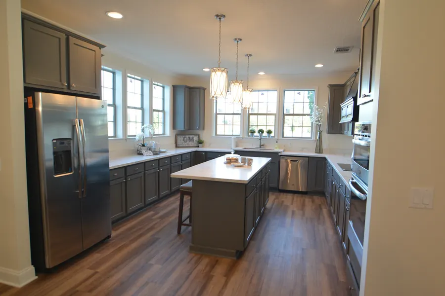 Kitchen with charcoal gray cabinets, stainless refrigerator and a large island under pendant lights