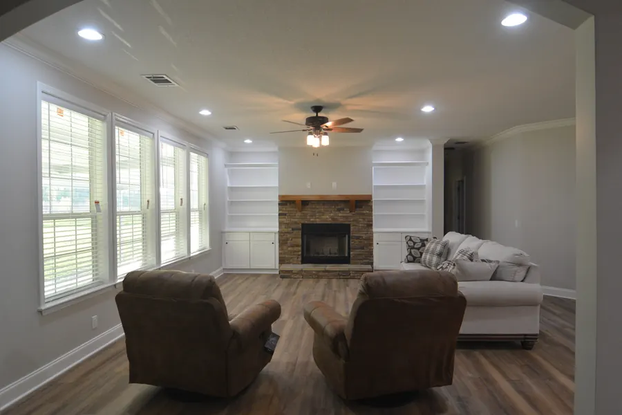 Bright living room with a stone fireplace, white built-in shelves and a wall of windows