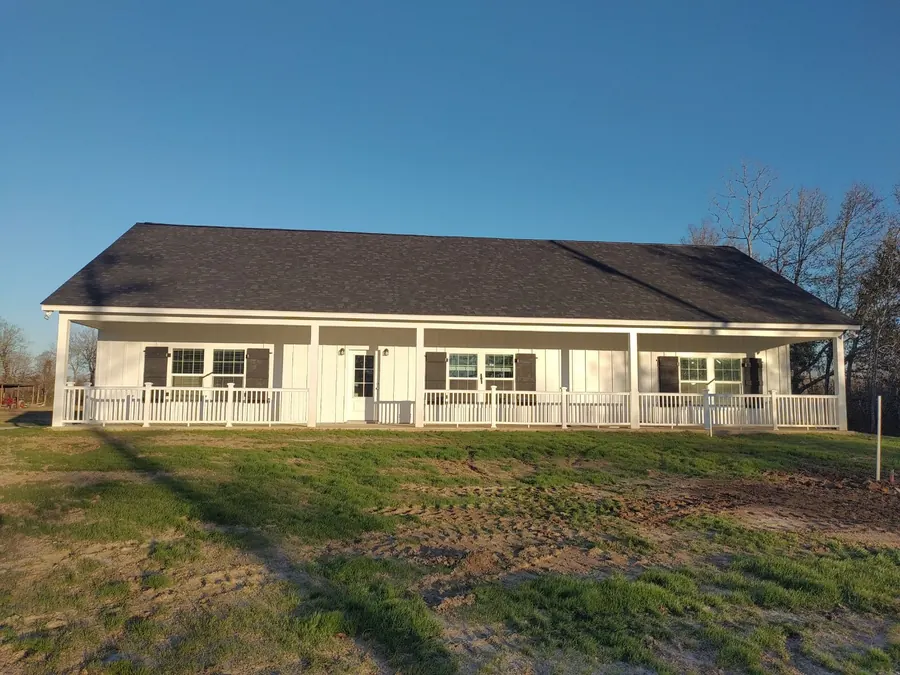 White home with dark shingle roof and a long railed front porch, just finished
