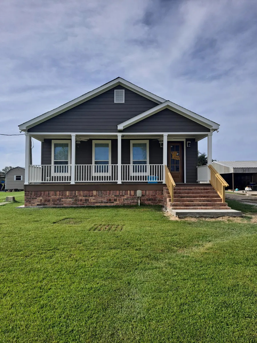 Navy-blue cottage with a white-railed front porch raised on a brick foundation