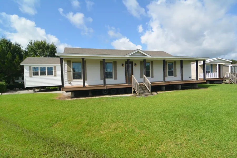 Long white home with a full-length covered front porch and steps on a green lawn